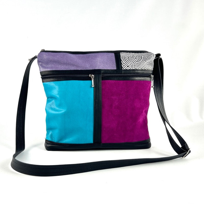A leather cross-body handbag with blue, purple, and black colors, featuring a zipper closure, an adjustable shoulder strap, and multiple zippered compartments.